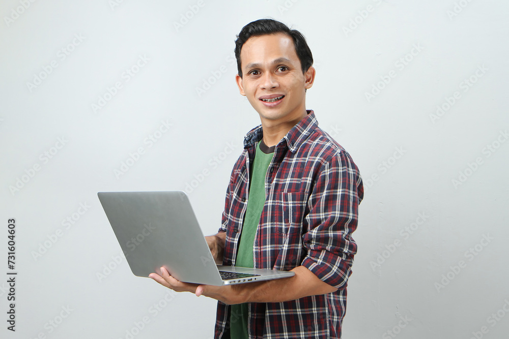Happy asian indonesian man holding laptop computer on isolated background Happy asian indonesian man holding laptop computer on isolated background
