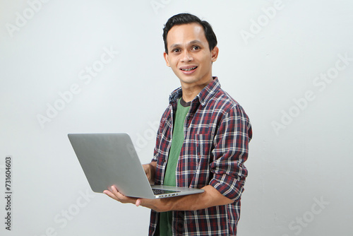 Happy asian indonesian man holding laptop computer on isolated background