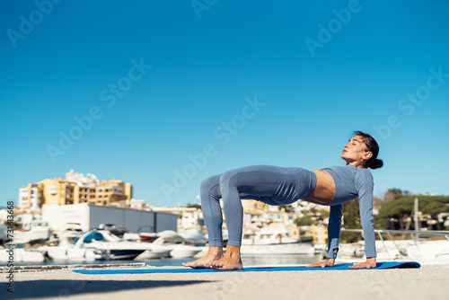 a sporty girl in sportswear is warming up on the pier against the backdrop of the sea, doing an exercise, stretching. fitness instructor shows exercise. motivation for sports and a healthy lifestyle