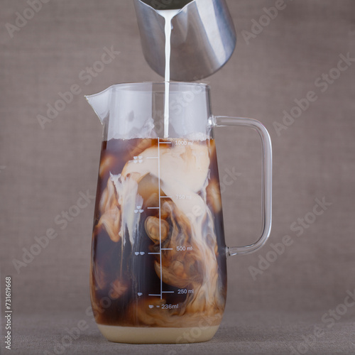 The process of pouring milk into a glass measuring jug with coffee.