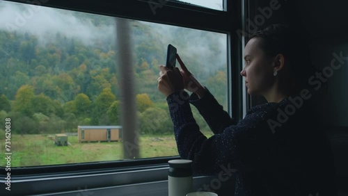 Young woman in train. Girl takes photo of mountain landscape outside the window while sitting inside transport. Passenger or traveler takes photos with phone. Woman taking pictures of Carpathian