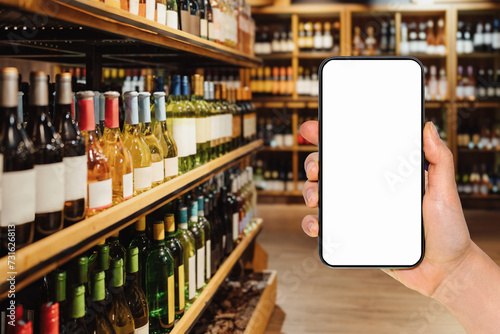 Smart phone with empty screen in female's hand in front of liquor store. Online ordering and shopping of alcohol drinks. Mockup for mobile app. photo