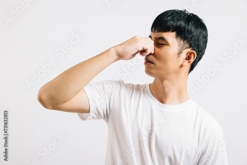 A disgusted Asian man holds his nose, expressing strong displeasure due to a bad smell situation. Studio shot isolated on white background, showcasing his humorous reaction.