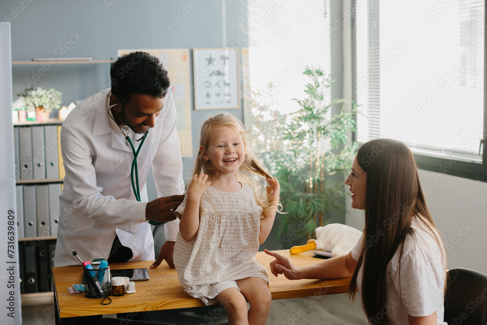 Mother and child seeing family practitioner. Smiling pediatrician with stethoscope checking little girl's lungs. Mother and child seeing family practitioner. Smiling pediatrician with stethoscope checking little girl's lungs.