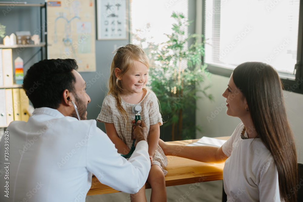 © dsheremeta - Mother and child seeing family practitioner. Smiling pediatrician with stethoscope checking little girl's lungs.