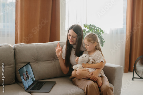 A young mother with her little daughter consults with her family doctor online using a laptop.