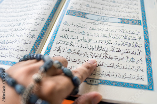 фотографія Close up Asian man's hand with tasbih beads pointing at Qur'an