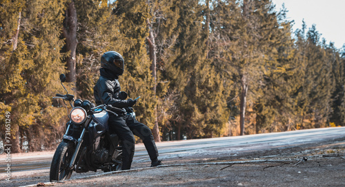 male motorcyclist in a classic retro motorcycle stands by a forest road in a leather jacket