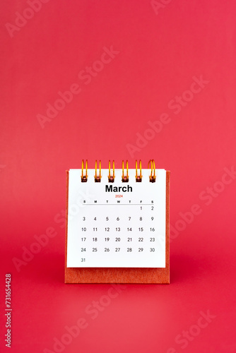March 2024 white mini desk calendar on red background.