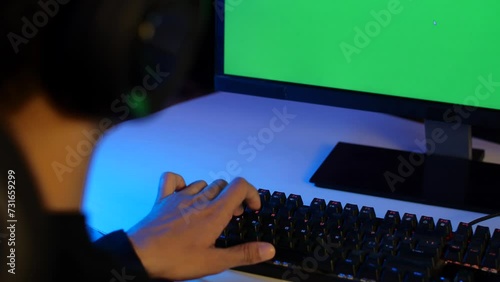 A young indian man focused on a computer with green chroma key screen - free ad space  video insert  green screen. Closeup shot of a gaming keyboard - professional gaming  gaming setup