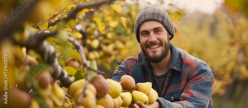 A happy man with a beard is picking natural foods from a tree in an orchard, enjoying the staple food and smiling. photo