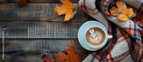 Top view of a cozy autumn theme with a woolen plaid, autumn leaves, and a coffee cup on a wooden table.