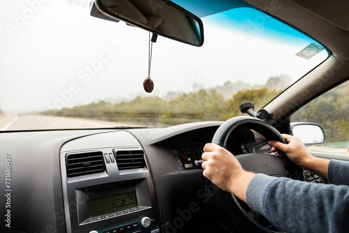 Man's hands on car steering wheel driving in foggy conditions photo