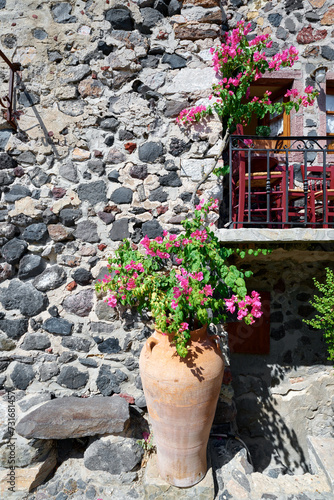 Beautiful vintage balcony with colorful flowers, terracotta pot, red chairs and natural stone wall in a narrow street of Pyrgos Kallistis village, Santorini. Greek Islands, European Vacation. 