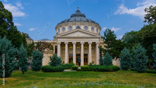 Romanian Athenaeum in Bucharest tall trees and bright green shrubs in the garden