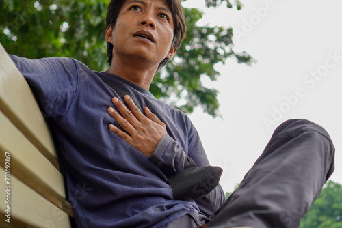 A handsome man is sitting on a bench holding his chest.