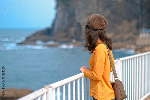 秋の海を眺めるオレンジ色のスウェットシャツを着た女性 © Nostalgico
