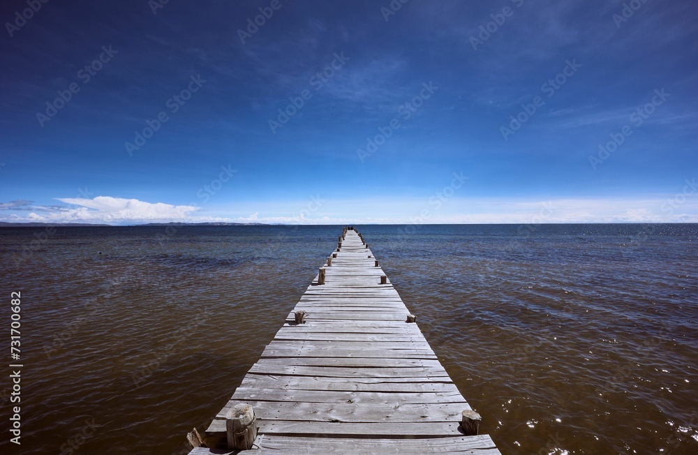Scenic view of a wooden dock extending over a tranquil ocean with a clear sky above.