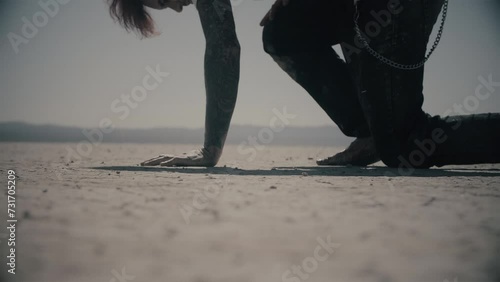Never give up. Exhausted barefoot man walking through desert in pain and falls on his knee. Guy gets up and keep walking. Cinematic shot in slow motion. Dry lake. Cold color correction, 4k