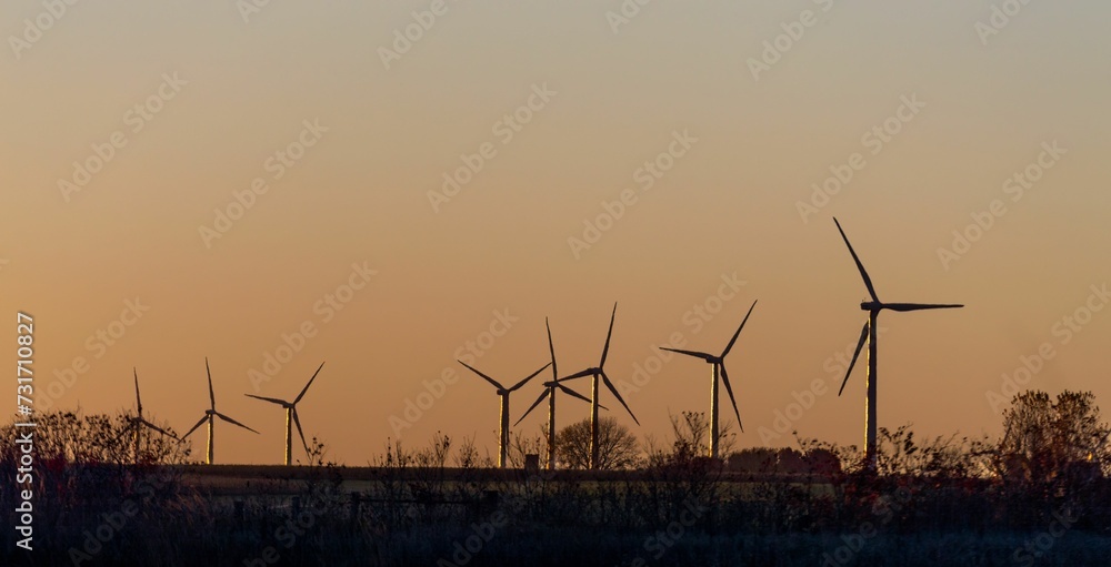 Field with multiple wind turbines silhouetted against the backdrop of a vibrant sunset sky