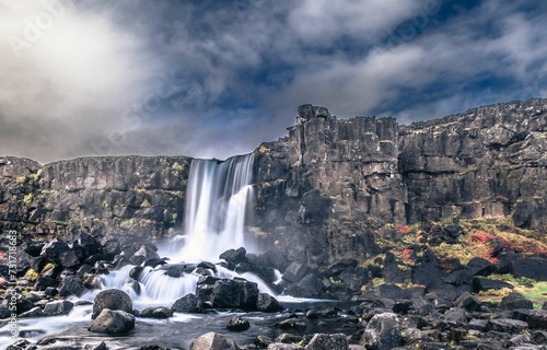 Scenic view of a large waterfall cascading into a body of water surrounded by rocky terrain