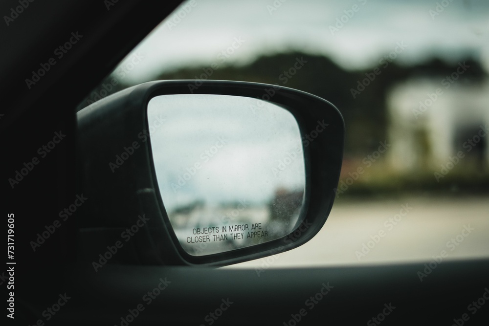 Side view mirror of a car, revealing the side and driver of the vehicle Side view mirror of a car, revealing the side and driver of the vehicle