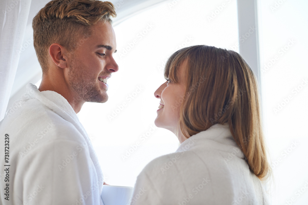 Couple, morning and happy in robe together with love, smile and eye contact in home or honeymoon. Man, woman and partnership with trust by window in house, connect and romance relationship with care Couple, morning and happy in robe together with love, smile and eye contact in home or honeymoon. Man, woman and partnership with trust by window in house, connect and romance relationship with care