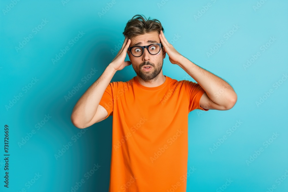 A man wearing an orange shirt is shown in profile, holding his head with both hands in a gesture of distress or frustration. A man wearing an orange shirt is shown in profile, holding his head with both hands in a gesture of distress or frustration.