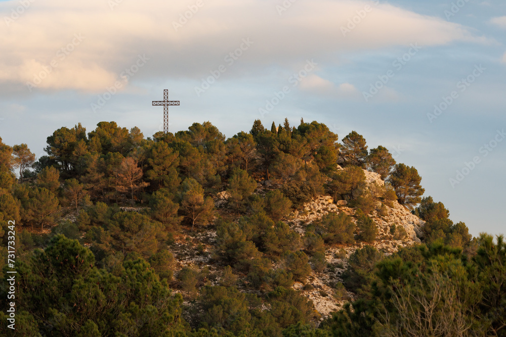 Paisaje de la colina de San Cristobal coronando con cruz religiosa metalica en las ultimas luces del día, Alcoy, España