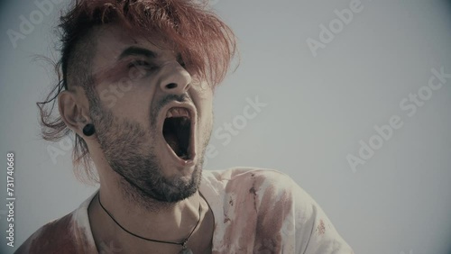 Badly wounded man screaming in pain. Loud screams. Vengeance and anger. Screaming in the desert. Loud shouts in the middle of nowhere. Bleeding mouth and bleeding person screaming. Cold color. photo