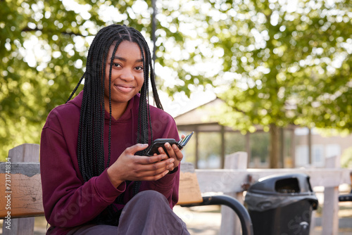 Young woman with braided hair holding smartphone in park photo