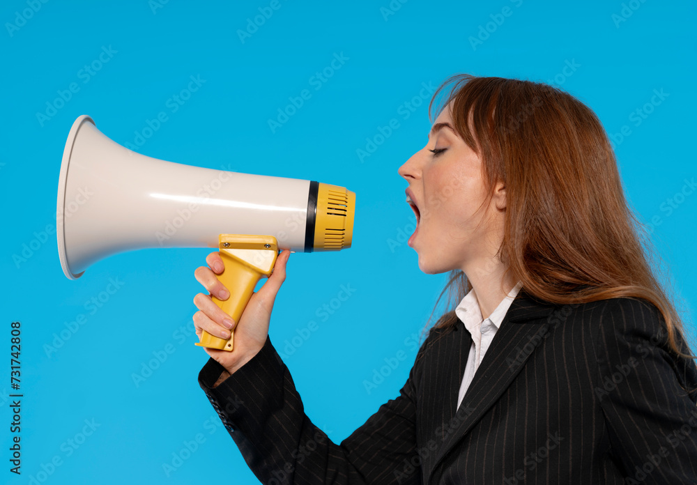 Woman in smart jacket making an announcement with a megaphone on blue background. People have sincere emotions, lifestyle concepts. Mock-up copy space. Screaming in megaphone Woman in smart jacket making an announcement with a megaphone on blue background. People have sincere emotions, lifestyle concepts. Mock-up copy space. Screaming in megaphone