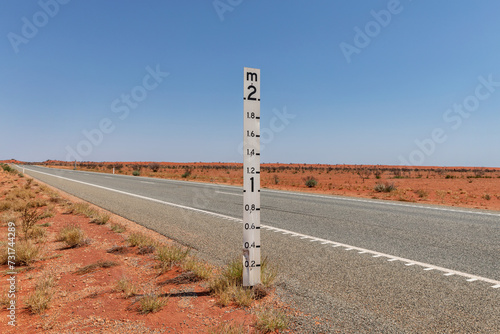 2 metre flood level marker on the edge of a long road crossing red, dry flood plain photo