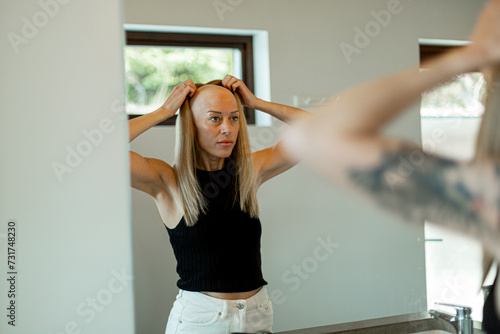 Reflection of bald woman wearing wig standing in bathroom at home photo