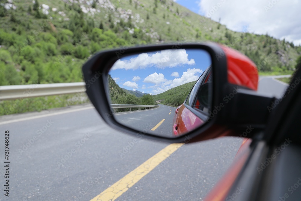 Closeup shot of a car's side mirror reflecting the road and green mountains.