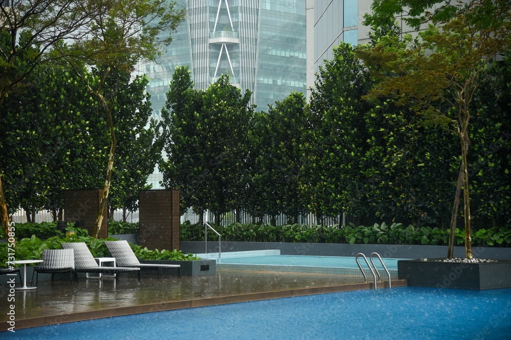 Pool surrounded by trees in a city courtyard next to the modern hotel on a rainy day