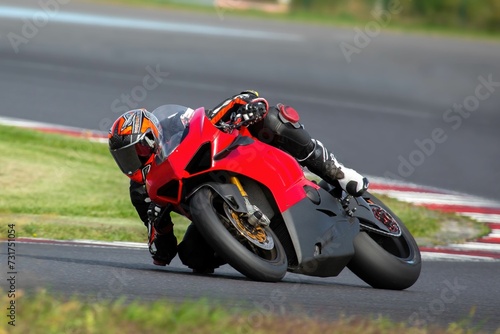 Young adult male is driving a red sports motorcycle on a sharp corner during the race © Wirestock
