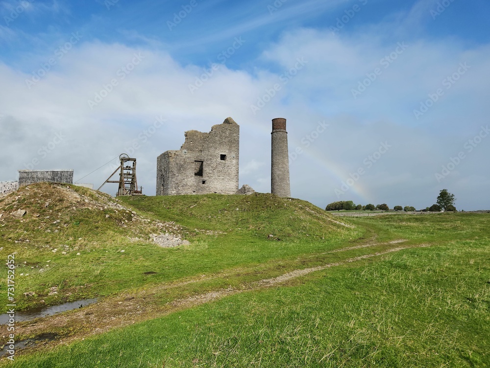 the remains of an old abandoned castle standing on a grassy hill with a rainbow