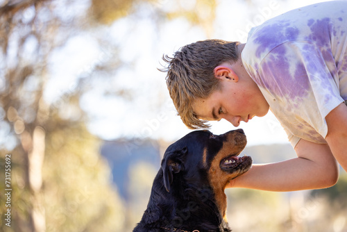 Teen boy showing affection to sitting rottweiler dog photo
