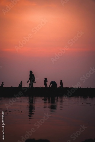 Beautiful view of the sunset sky over the shore with silhouettes of people enjoying it © Wirestock