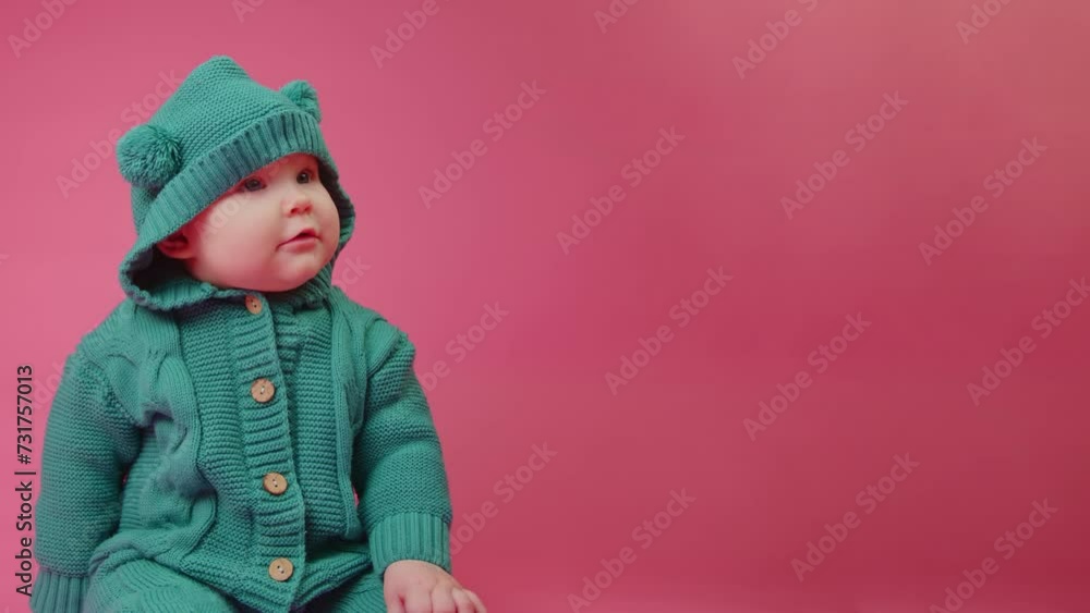 Portrait of a cute baby in a warm knitted jumpsuit with a hood on a pink background Portrait of a cute baby in a warm knitted jumpsuit with a hood on a pink background