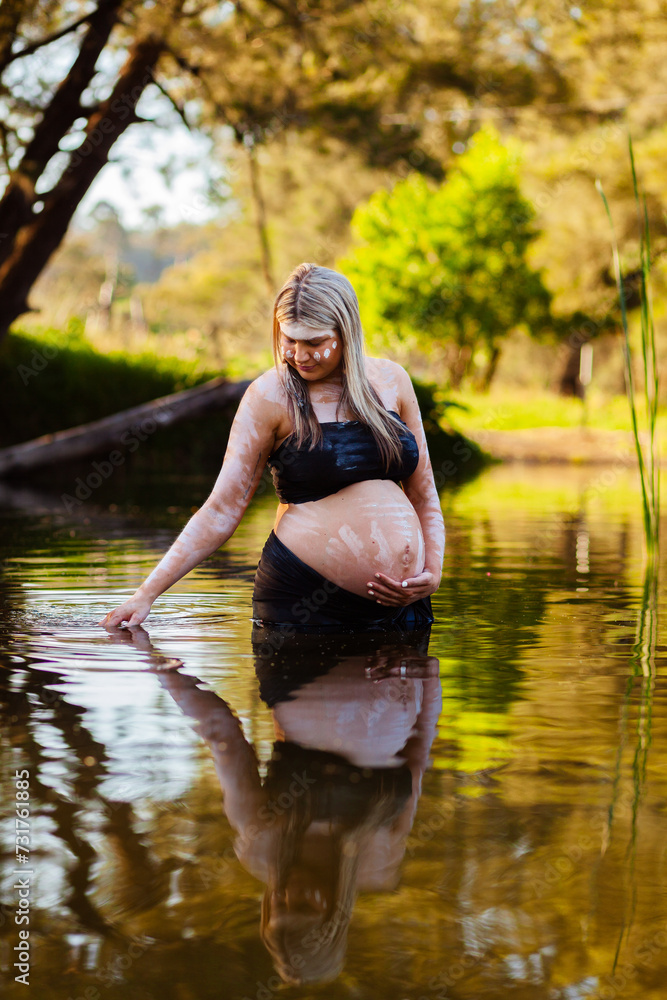 Pregnant Aboriginal Australian woman in traditional ochre body paint standing in creek Pregnant Aboriginal Australian woman in traditional ochre body paint standing in creek