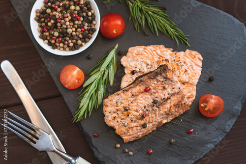 Grilled red fish meat salmon steak with tomato rosemary and spices on black stone background