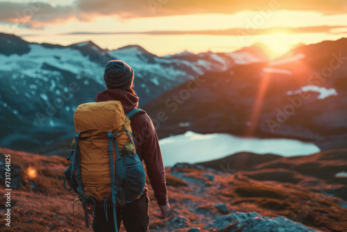 Close up back view of young man with a travel backpack on his back stands on mountain at sunset. Joyful free travel concept photo