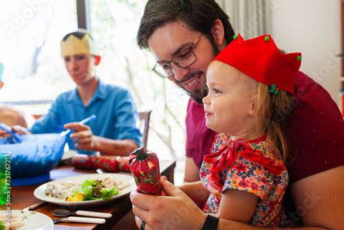 Toddler girl with popped Christmas cracker at lunch with family photo