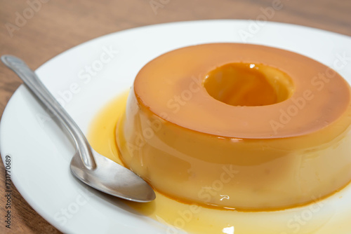 pudim de leite, or pudding also known as flan on a wooden table with metallic spoon