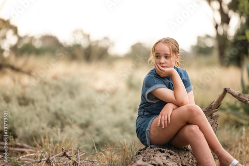 Portrait of pre-teen girl sitting on log in natural setting with thoughtful expression photo
