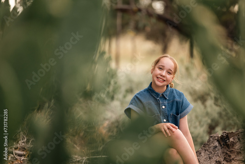 Portrait of pre-teen girl sitting on log in natural setting with big smile photo