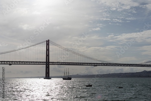 Scenic view of a boat sailing under a bridge on a cloudy day