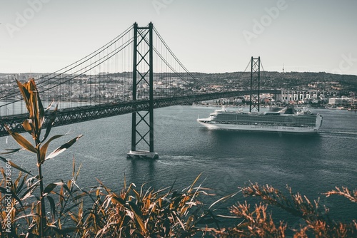 Cargo ship emerging from under the iconic 25 April Bridge in Lisbon, Portugal photo